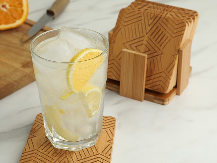 White Marble slab with light oak wood coasters and a glass of ice lemon water